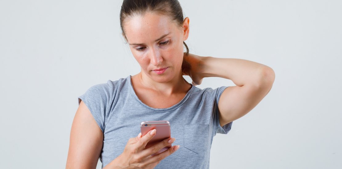 Young female using mobile phone with hand on neck in grey t-shir