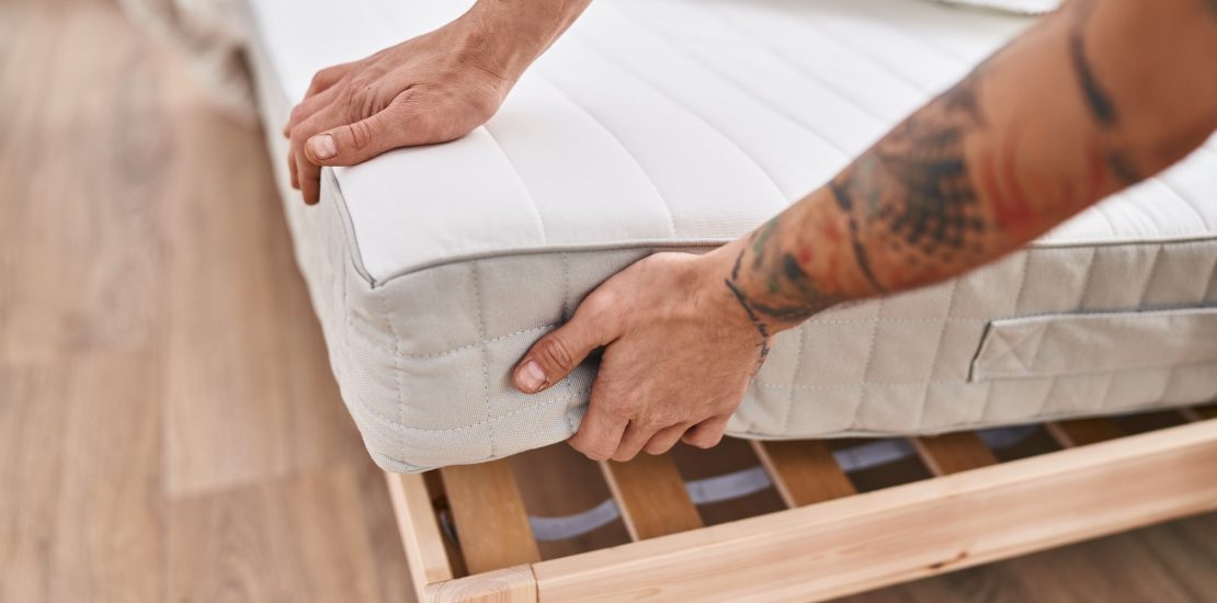 Young man holding mattress at bedroom